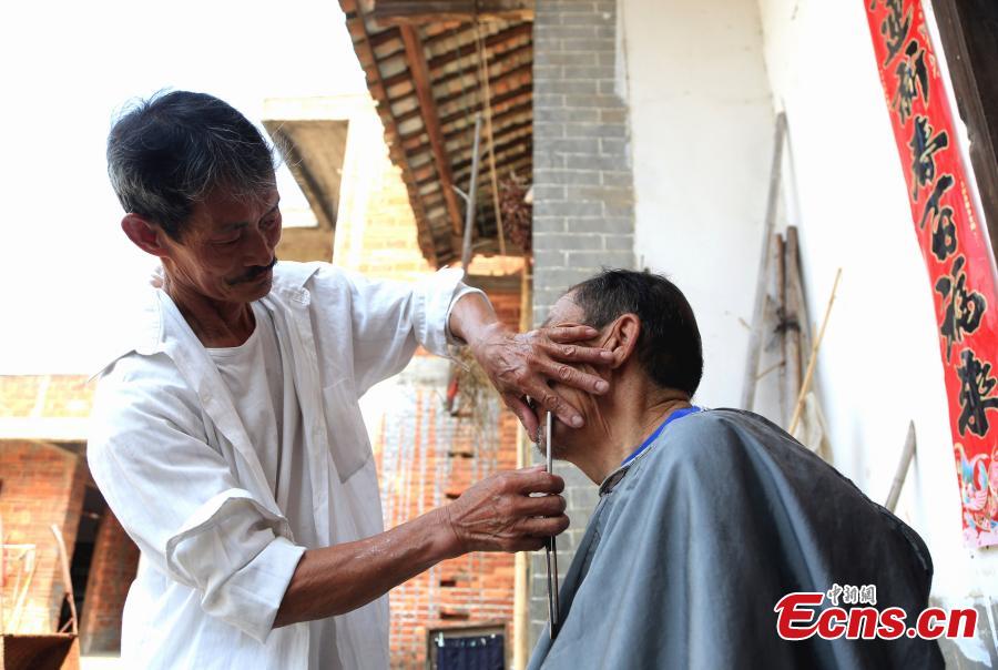 Barber Hu Daofa cuts a man’s hair at a village in Zhuangbu Countryside, Huichang County, East China’s Jiangxi Province. Hu, 73, started travelling around nearby villages offering door-to-door haircutting, shaving, and ear-cleaning in 1966, charging an annual fee of 130 yuan for three visits a month. Hu can’t ride a bicycle, so he walks. Most of his customers are children and elderly people. (Photo: China News Service/Jiang Tao)