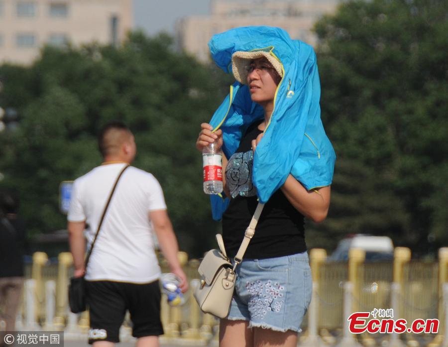 Tourists try all possible ways, including wearing hats, to shade themselves from the sun near the Forbidden City and Tiananmen Square in Beijing, March 31, 208, as temperatures rose to a record 35 degrees centigrade. Beijing issued a yellow alert against high temperatures on Thursday. (Photo/VCG)