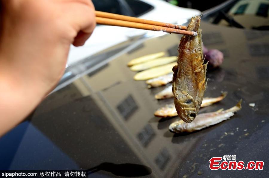 A woman grills fish, meat, potato slices and sweet potato on the bonnet of a car in Binzhou City, East China’s Shandong Province, June 5, 2018, as temperatures rise to nearly 40 degrees centigrade. It took half an hour to cook the fish. (Photo/SipaPhoto)