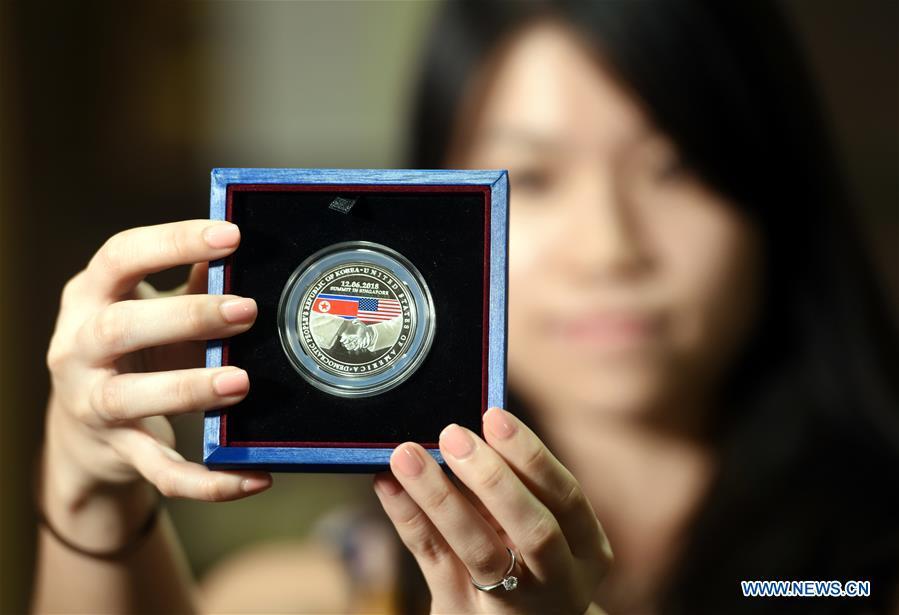 A staff member displays a sample of the medallion presented by the Singapore Mint on the occasion of the summit between U.S. President Donald Trump and Kim Jong Un, top leader of the Democratic People\'s Republic of Korea (DPRK), in Singapore, on June 11, 2018. (Xinhua/Qin Qing)