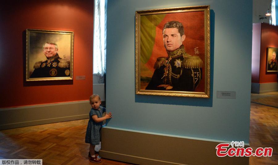 A child walks in front of portraits of Manchester United\'s former Scottish Manager Sir Alex Ferguson (L) and Portugal football player Cristiano Ronaldo (R) as they attend during the Art Project \'Like the Gods\', presented by the Museum of the Russian Academy of Arts and Italian artist Fabrizio Birimbelli during the Russia 2018 World Cup in Saint Petersburg, on June 20, 2018. The project presents a series of portraits of world football stars and coaches in historical uniforms and includes more than 40 portraits. (Photo/Agencies)