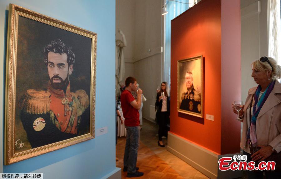 A portrait of Egyptian football player Mohamed Salah (L) is on display as visitors attend the opening of the Art Project \'Like the Gods\', presented by the Museum of the Russian Academy of Arts and Italian artist Fabrizio Birimbelli during the Russia 2018 World Cup in Saint Petersburg, on June 20, 2018. The project presents a series of portraits of world football stars and coaches in historical uniforms and includes more than 40 portraits. (Photo/Agencies)
