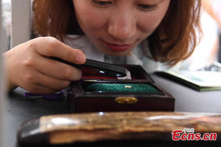A visitor uses a magnifying glass to look at a piece of work by Pan Qihui at an exhibition in Chongqing, June 23, 2018. The smallest characters carved by Pan are as thin as a hair and a magnifying glass is needed to see them. (Photo: China News Service/Chen Chao)