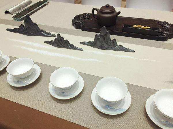 A tea table at the First Exchange of Tea Culture Between Beijing and Taiwan, Beijing, June 24, 2018. (Photo provided to chinadaily.com.cn)

An exquisite porcelain teapot. Several fine ceramic cups. A small vase and a flower. A piece of calligraphy introducing tea making procedures.

These fives things adorn a traditional Chinese tea table. With a touch of Chinese aesthetic, the table is almost an artwork in the form of modern installation.

Another piece was inspired by A Thousand Miles of Rivers and Mountains, a masterpiece by Song Dynasty (960-1279) painter Wang Ximeng. The painting was featured on cups and table flag which were decorated with black mountain-shaped sculptures.

A total of 30 such tables, from both Chinese mainland and Taiwan, were featured at the First Exchange of Tea Culture Between Beijing and Taiwan at Grand Millennium Beijing on June 24.