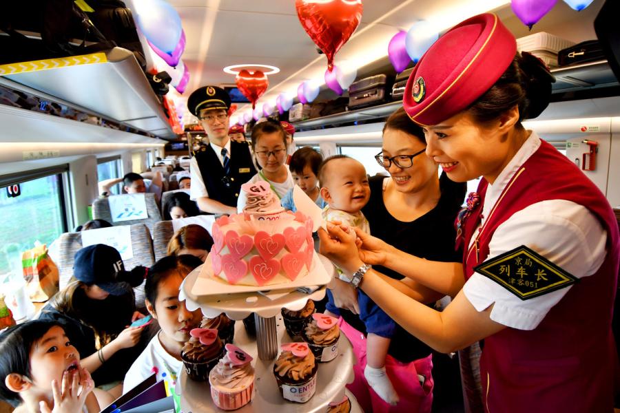 A steward holds a baby passenger\'s hands to cut the birthday cake on the G1 Fuxing high-speed bullet train on Beijing-Shanghai high speed railway line on June 26, 2018. (Photo/Xinhua)