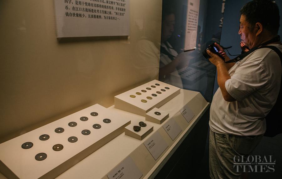 A visitor takes a photo of gold, silver and bronze coins minted with characters that read \