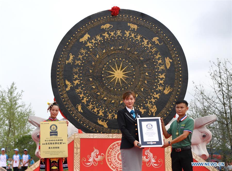Staff demonstrate certificates beside a gigantic bronze drum in Huanjiang Maonan Autonomous County, south China\'s Guangxi Zhuang Autonomous Region, June 29, 2018. The drum measures 6.68 meters in diameter and weighs 50 tons. It was recognized as the largest bronze drum by Guinness World Records. (Xinhua/Zhou Hua)
