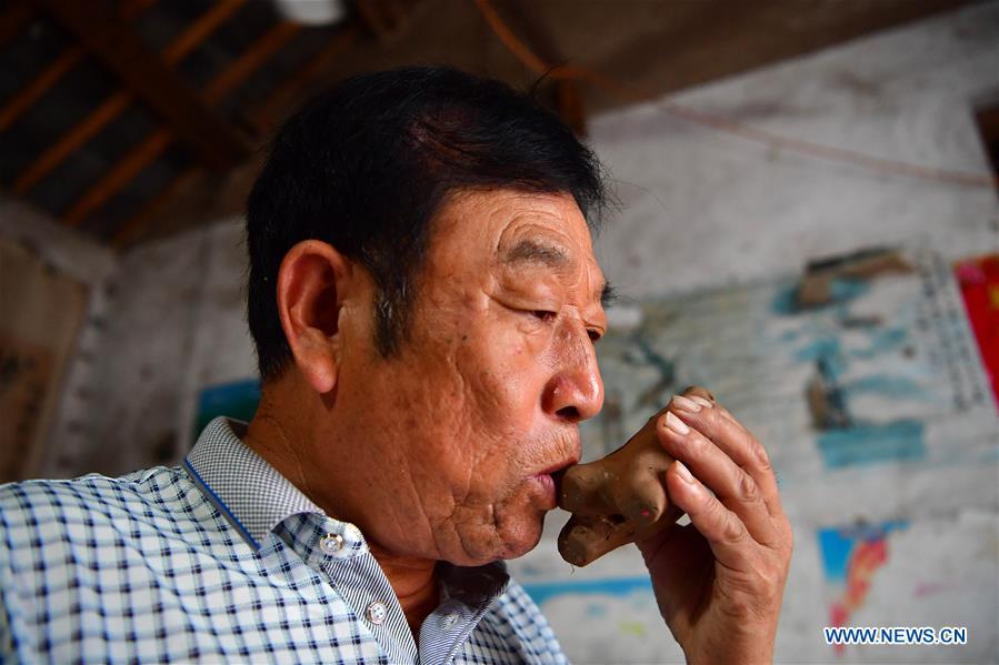 Local handicraftsman Ren Guohe blows a whistle-shaped clay statuette in Jinzhuang Village of Huaiyang County, central China\'s Henan Province, July 9, 2018. Originated from ancient sacrificial ceremonies, the hand-made clay statuette \