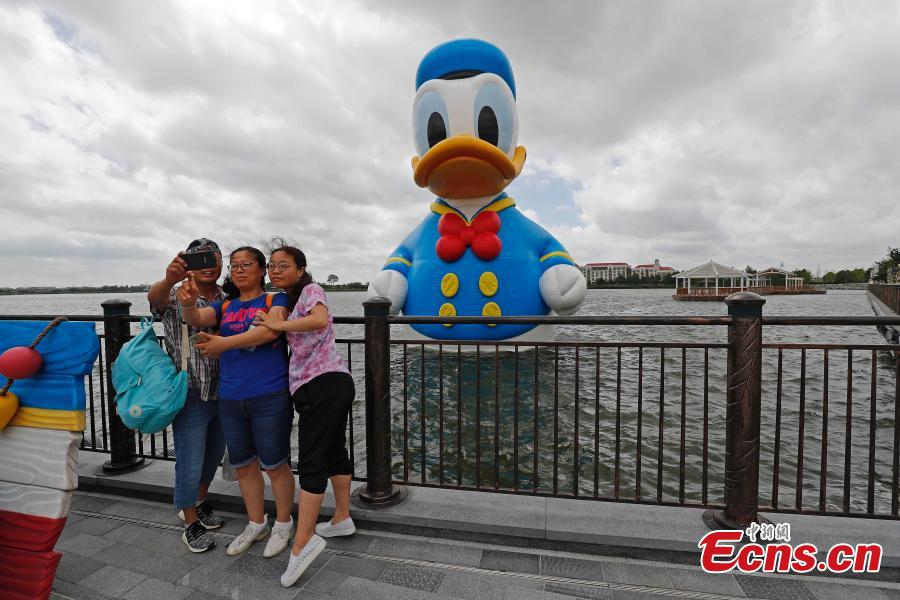 <?php echo strip_tags(addslashes(Visitors pose for photos with an 11-meter-tall Donald Duck in Wishing Star Lake at the Shanghai Disney Resort, July 12, 2018. (Photo/China News Service))) ?>