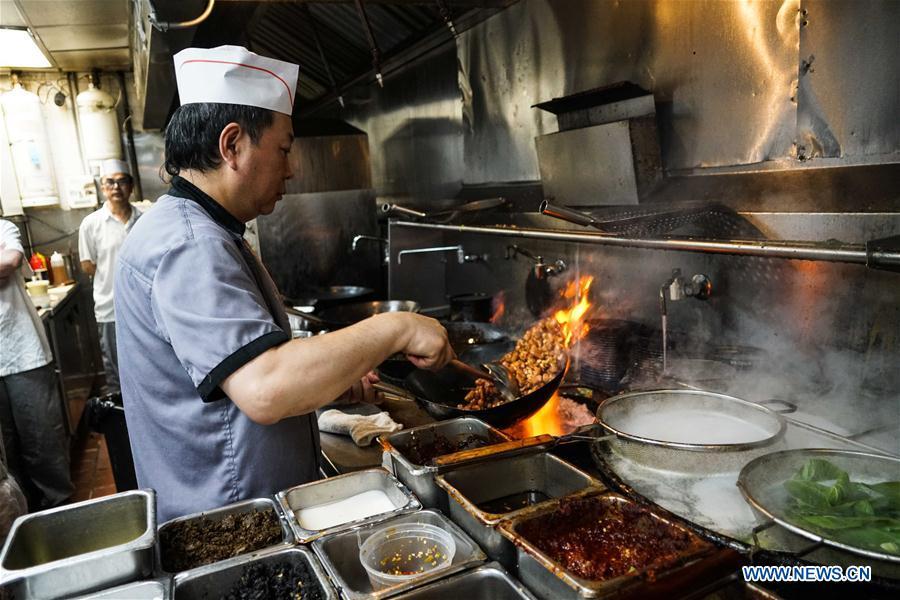 A chef cooks Kung Pao Chicken at Cafe China in New York, the United States, on June 27, 2018. Walking in the bustling street of midtown Manhattan, you may not notice Cafe China if there weren\'t so many people waiting for seats outside the Chinese restaurant. Although the space is limited and decoration not so luxury, Cafe China has won Michelin one star for six consecutive years from 2012 to 2017. Wang Yiming and Zhang Xian, a couple from China, quit their well-paid financial jobs in New York and opened Cafe China with the ambition to provide authentic Sichuan cuisine along with a comfortable dining environment. They decided not to sell American-Chinese dishes like most Chinese restaurants did at that time. Meanwhile, the couple decorated the place with items such as vintage posters, antique cameras and lamps to create an old Shanghai style. At the beginning, their idea was strongly opposed by many friends and even their staff, as the American-Chinese food was the easiest way to make money at that time. However, it surprised them that many Americans swarmed to Cafe China with curiosity for decent Chinese dishes and the unique dining environment as soon as the restaurant just opened. The couple believed the success of Cafe China resulted from not only the appeal of authentic Chinese food but also the sophisticated Chinese culture behind it. \