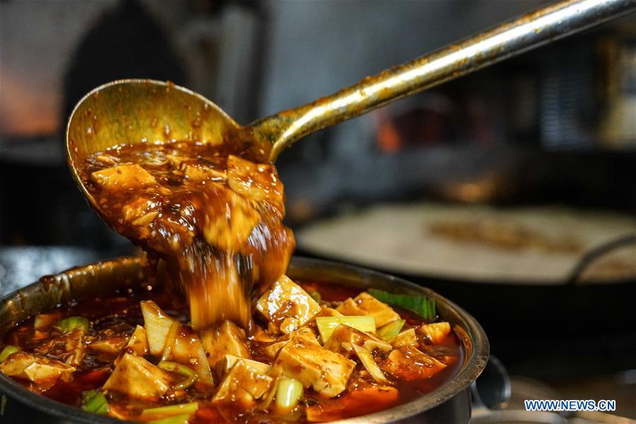A chef pours Mapo tofu to a container at Cafe China in New York, the United States, on June 27, 2018. Walking in the bustling street of midtown Manhattan, you may not notice Cafe China if there weren\'t so many people waiting for seats outside the Chinese restaurant. Although the space is limited and decoration not so luxury, Cafe China has won Michelin one star for six consecutive years from 2012 to 2017. Wang Yiming and Zhang Xian, a couple from China, quit their well-paid financial jobs in New York and opened Cafe China with the ambition to provide authentic Sichuan cuisine along with a comfortable dining environment. They decided not to sell American-Chinese dishes like most Chinese restaurants did at that time. Meanwhile, the couple decorated the place with items such as vintage posters, antique cameras and lamps to create an old Shanghai style. At the beginning, their idea was strongly opposed by many friends and even their staff, as the American-Chinese food was the easiest way to make money at that time. However, it surprised them that many Americans swarmed to Cafe China with curiosity for decent Chinese dishes and the unique dining environment as soon as the restaurant just opened. The couple believed the success of Cafe China resulted from not only the appeal of authentic Chinese food but also the sophisticated Chinese culture behind it. \