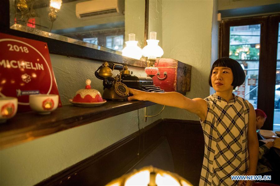 Restaurant owner Wang Yiming arranges decorations at Cafe China in New York, the United States, on June 27, 2018. Walking in the bustling street of midtown Manhattan, you may not notice Cafe China if there weren\'t so many people waiting for seats outside the Chinese restaurant. Although the space is limited and decoration not so luxury, Cafe China has won Michelin one star for six consecutive years from 2012 to 2017. Wang Yiming and Zhang Xian, a couple from China, quit their well-paid financial jobs in New York and opened Cafe China with the ambition to provide authentic Sichuan cuisine along with a comfortable dining environment. They decided not to sell American-Chinese dishes like most Chinese restaurants did at that time. Meanwhile, the couple decorated the place with items such as vintage posters, antique cameras and lamps to create an old Shanghai style. At the beginning, their idea was strongly opposed by many friends and even their staff, as the American-Chinese food was the easiest way to make money at that time. However, it surprised them that many Americans swarmed to Cafe China with curiosity for decent Chinese dishes and the unique dining environment as soon as the restaurant just opened. The couple believed the success of Cafe China resulted from not only the appeal of authentic Chinese food but also the sophisticated Chinese culture behind it. \