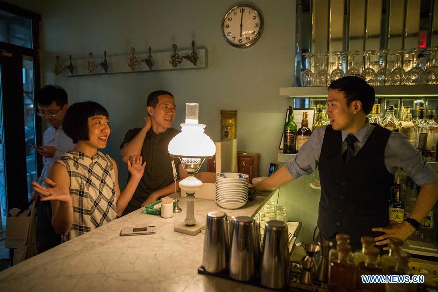 Restaurant owner Wang Yiming (3rd R) and Zhang Xian (2nd R) talk with a bartender at Cafe China in New York, the United States, on June 27, 2018. Walking in the bustling street of midtown Manhattan, you may not notice Cafe China if there weren\'t so many people waiting for seats outside the Chinese restaurant. Although the space is limited and decoration not so luxury, Cafe China has won Michelin one star for six consecutive years from 2012 to 2017. Wang Yiming and Zhang Xian, a couple from China, quit their well-paid financial jobs in New York and opened Cafe China with the ambition to provide authentic Sichuan cuisine along with a comfortable dining environment. They decided not to sell American-Chinese dishes like most Chinese restaurants did at that time. Meanwhile, the couple decorated the place with items such as vintage posters, antique cameras and lamps to create an old Shanghai style. At the beginning, their idea was strongly opposed by many friends and even their staff, as the American-Chinese food was the easiest way to make money at that time. However, it surprised them that many Americans swarmed to Cafe China with curiosity for decent Chinese dishes and the unique dining environment as soon as the restaurant just opened. The couple believed the success of Cafe China resulted from not only the appeal of authentic Chinese food but also the sophisticated Chinese culture behind it. \