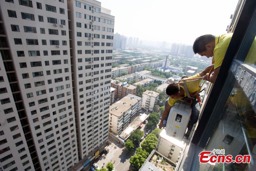A man, attached to a rope, installs air-conditioning equipment on the outside of a tall building in Taiyuan City, North China’s Shanxi Province, July 20, 2018. (Photo: China News Service/Zhang Yun)