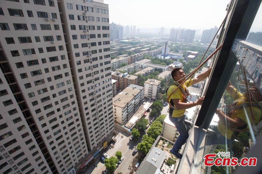 A man, attached to a rope, installs air-conditioning equipment on the outside of a tall building in Taiyuan City, North China’s Shanxi Province, July 20, 2018. (Photo: China News Service/Zhang Yun)