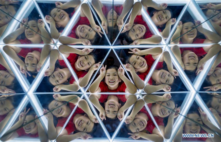 A girl plays in front of a mirror in the Inner Mongolia Science and Technology Museum in Hohhot, north China\'s Inner Mongolia Autonomous Region, July 27, 2018. Children take part in various classes and activities to enrich their summer vacation life. (Xinhua/Ding Genhou)