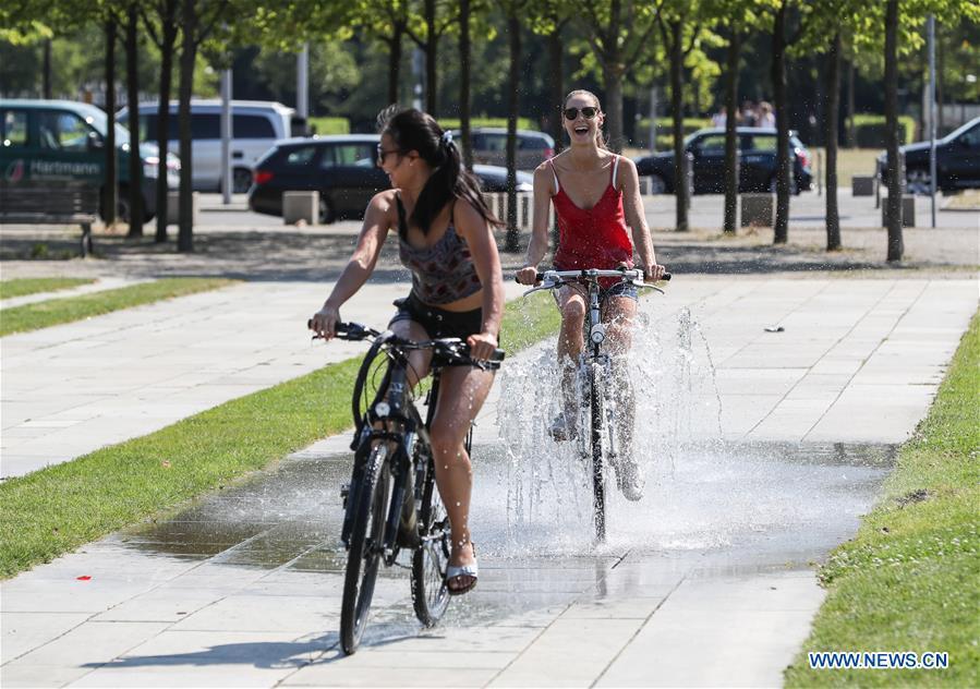 Cyclists ride through a fountain to cool off in Berlin, capital of Germany, on Aug. 3, 2018. As Europe\'s scorching heat wave continues to spread across the continent, forecasters are now saying the all-time temperature record in Europe could be broken in the coming days. (Xinhua/Shan Yuqi)