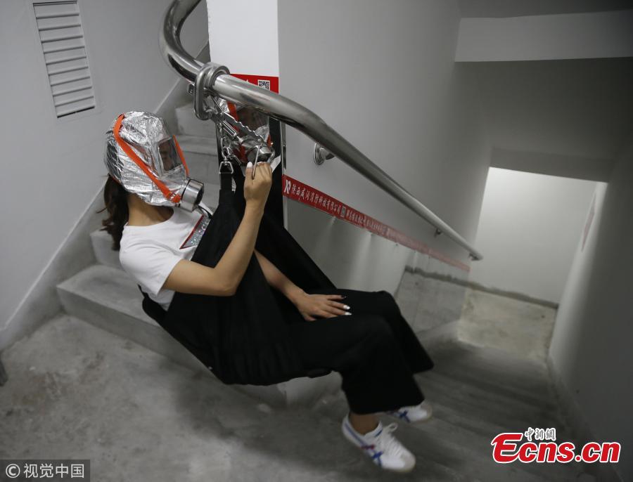 An emergency escape system designed for use in high-rise buildings was unveiled in Xi\'an, Shaanxi Province on Wednesday. If a fire breaks out, people can glide down through the stairwell at a speed of around 1 meter per second using a special railing that can bear the weight of a 100 kilogram person. The emergency exit also has respirators to protect evacuees from poisonous dust and gases. In this photo taken on Wednesday, August 22, 2018 two staff members from the developer of the system demonstrate how it is used. (Photo/VCG)