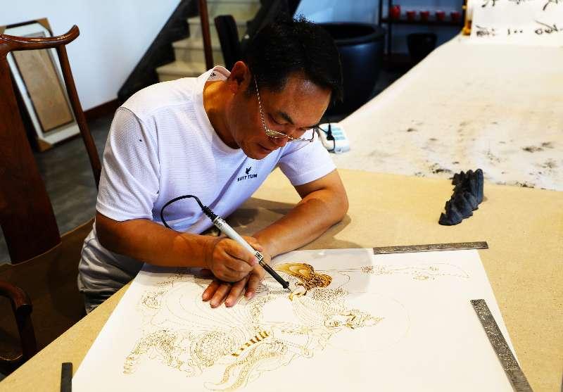Zhang Ge guides a woodburning pen to create a pyrography artwork.  (Photo provided to chinadaily.com.cn)

Zhang Ge, an artist in Datong, North China\'s Shanxi Province, has created a series of pyrography, artworks themed on famous landscapes, historical figures and stories about the city, such as the Yungang Grottoes and Xuankong Temple.

Pyrography, or woodburning, is the art of decorating wood or other materials resulting from the controlled application of a heated object, such as a woodburning pen.

\