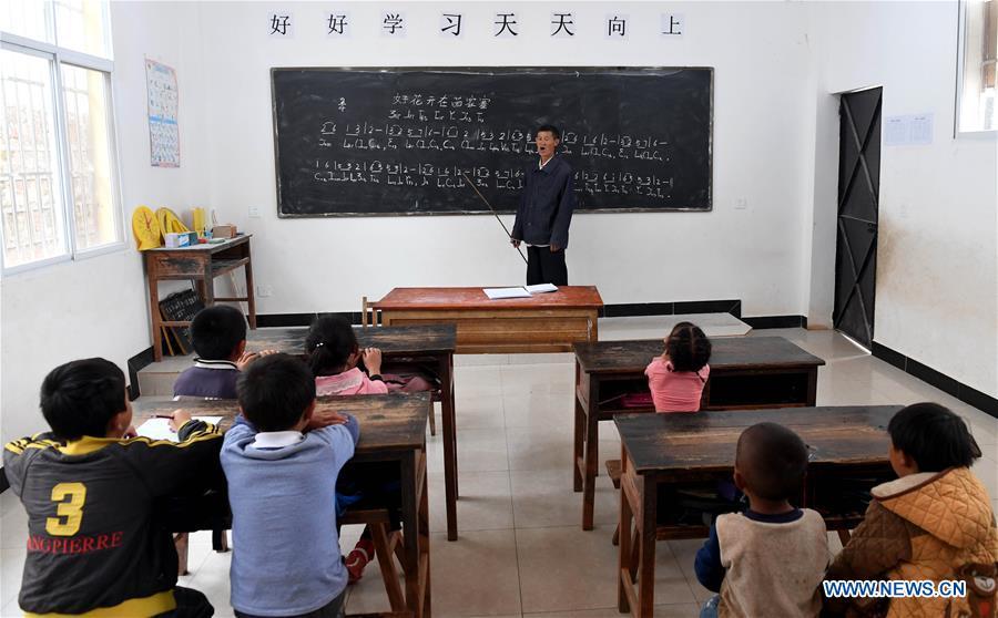 Wang Zhengxiang teaches music to students at Ayiyang Primary School in Sanmeng Village of Luquan Yi and Miao Autonomous County, southwest China\'s Yunnan Province, Sept. 6, 2018. One teacher, eight students, none was and will be given up thanks to rural teacher Wang Zhengxiang. Wang Zhengxiang of Miao ethnic group, 56, is the only teacher and has been teaching at the remote village primary school of Ayiyang for 38 years. Ayiyang Primary School, lying at an altitude of 2,600 meters above sea level and surrounded by mountains, is not within easy reach of outside world. There are just eight students at the school. Yet Wang takes care of his students with love, consideration and strong sense of responsibility. He buys shoes and daily goods for poverty-stricken students with his own money, and he has tried every means to keep those who wanted to drop out due to economic insufficiency. \