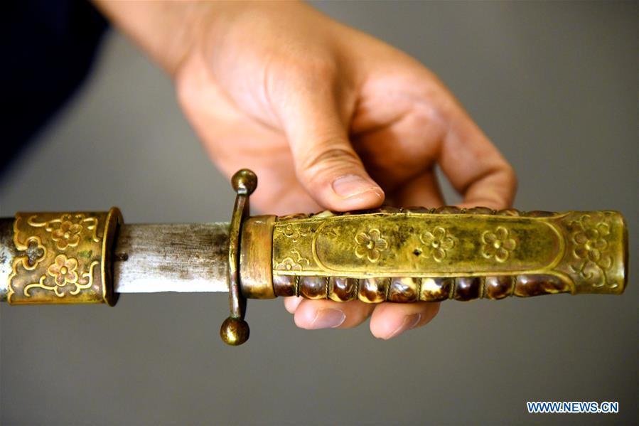 <?php echo strip_tags(addslashes(Yan Min displays a repaired ancient weapon in Shijiazhuang, north China's Hebei Province, Sept. 11, 2018. Yan Min, dedicated to ancient weapon restoration for more than 30 years, has hitherto repaired over 500 pieces of ancient weapons with his son Yan Peng. Influenced by his father, Yan Peng quit his job and embarked on restoring ancient weapons in the year of 2015. The sophisticated craftsmanship of ancient weapon restoration embodies working procedures of polishing, burnishing, grinding etc. 