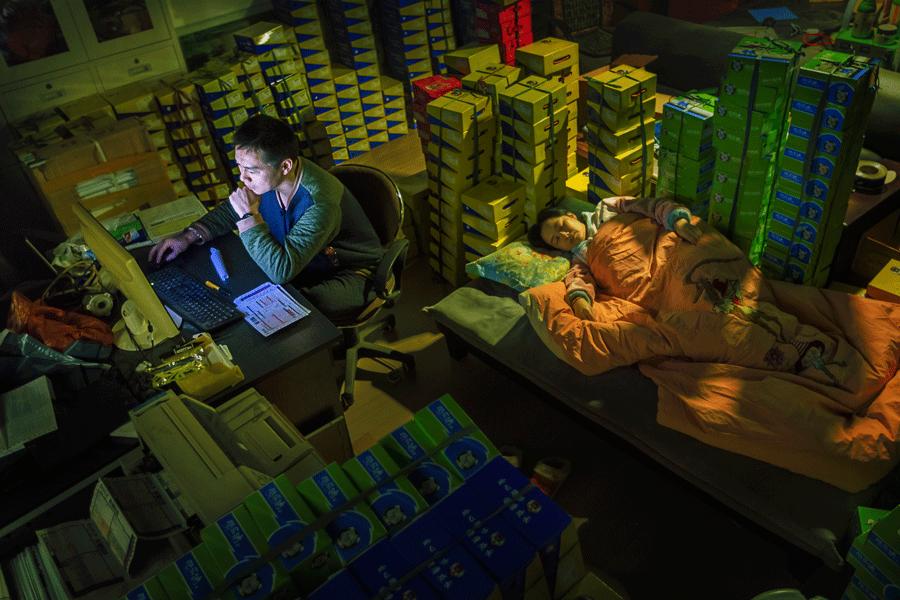 A man manages his e-commerce business at 1 am on Nov 12, 2014, in Wenzhou, Zhejiang province, while his wife sleeps. November 11 is an e-commerce discount day in China. [ZHAO YONG/FOR CHINA DAILY]