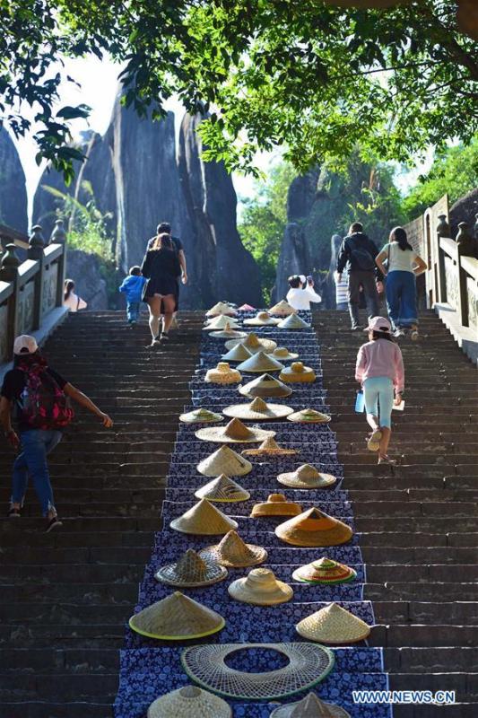 Tourists walk up stone steps decorated with bamboo rain hats at Yushilin scenic spot in Hezhou City, south China\'s Guangxi Zhuang Autonomous Region, Oct. 5, 2018. (Xinhua/Huang Xuhu)