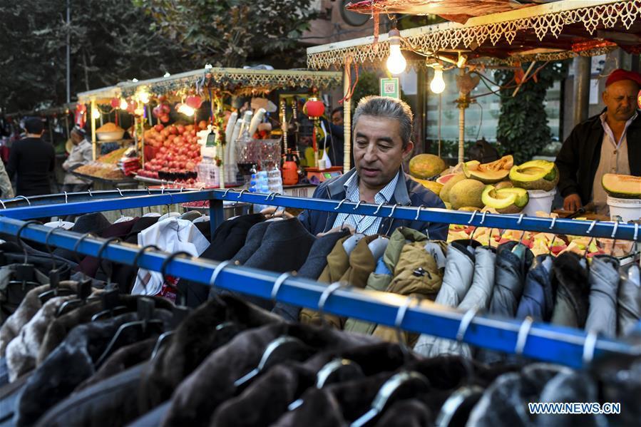 A resident chooses clothes at a night market in Kashgar City, northwest China\'s Xinjiang Uygur Autonomous Region, Oct. 16, 2018. The ancient oasis city of Kashgar, in the westernmost part of China near the border with Kyrgyzstan, Tajikistan, Afghanistan, and Pakistan, was an important staging post on the original Silk Road and has been revitalized as a bustling hub of business and different cultures. (Xinhua/Hu Huhu)