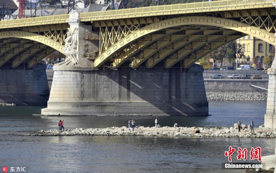 People stand on a dry flat of land, which is an extension of Margaret Island, temporarily exposed by the low water level of the River Danube at Margaret Bridge in Budapest, Hungary, Oct. 16, 2018. Due to the heat wave and lack of rainfall in the past period, the water level of the River Danube sank significantly in the region.(Photo/Agencies)