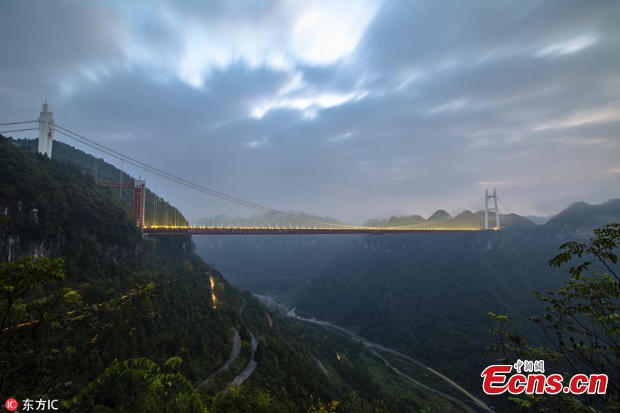 An early morning view of a winding road on a mountain and the Aizhai Bridge in Jishou City, Central China’s Hunan Province, Oct. 17, 2018. The suspension bridge was built as part of an expressway from southwest China\'s Chongqing Municipality to Changsha. The bridge links two tunnels 1,176 meters apart and carries traffic 330 meters above the floor of the Dehang Canyon, setting several records including the world\'s highest and longest tunnel-to-tunnel bridge. (Photo/IC)