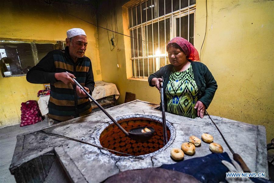 Yusup Tapuhan (L) and his wife bake butter naan in Yuli County of the Mongolian Autonomous Prefecture of Bayingolin, northwest China\'s Xinjiang Uygur Autonomous Region, Oct. 17, 2018. Yusup Tapuhan launched his butter naan business in 2000. The making of this popular pastry has been a tradition in Yuli County. In 2017, a dedicated local naan guild was established to help those in the business optimize profit. Yusup, who is 63, became one of the guild\'s earliest members. With the help of his family, Yusup can make 50 kilograms of butter naan and earn 500 yuan (72 U.S. dollars) a day. (Xinhua/Zhao Ge)