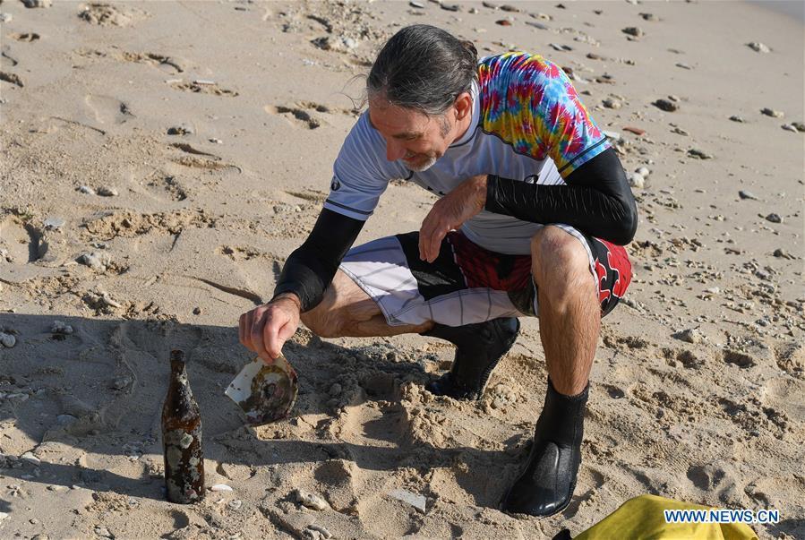 Canadian Craig Anderson looks at a waste porcelain and a bottle he picked up during a diving in the sea off the West Island in Sanya, south China\'s Hainan Province, Sept. 20, 2018. Anderson arrived in February at the West Island inhabited by around 4,000 people. Locals regarded Anderson as a scavenger when he first arrived, as he wandered around the beach almost every day, picking up driftwood, plastic bottles, shattered glasses, and rusty pieces of iron. As time went by, the locals realized that Anderson is an artist who devotes himself in environment protection art design. He profits the recyclable and regenerative materials in making art works. (Xinhua/Yang Guanyu)