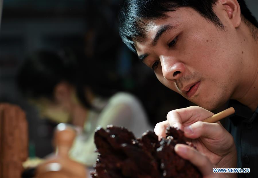 <?php echo strip_tags(addslashes(Lin Jianjun makes wood carving at a studio in Putian, southeast China's Fujian Province, Oct. 23, 2018. Lin Jianjun, who learnt wood carving at the age of 16, has studied the making skill of this traditional artwork for more than 20 years. In 2014, Lin got married with Chen Qin. The wife was influenced by her husband and got interested in wood carving. She developed the wood carving by combining a traditional skill to make wood carving inlaid with gold and silver. The couple meanwhile try to promote the Putian wood carving by giving lessons, instructing apprentices and displaying their works to the public. In 2018, Lin was appointed as the inheritor of the wood carving skill, a provincial-level intangible cultural heritage. (Xinhua/Zhang Guojun))) ?>