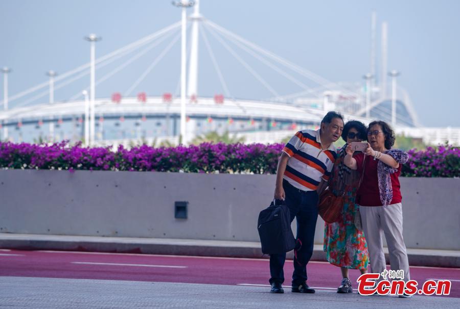 Passengers pose for a photo against the backdrop of the Zhuhai-Hong Kong-Macao Bridge at the Zhuhai Port, Oct. 24, 2018. (Photo: China News Service/Zhang Wei)