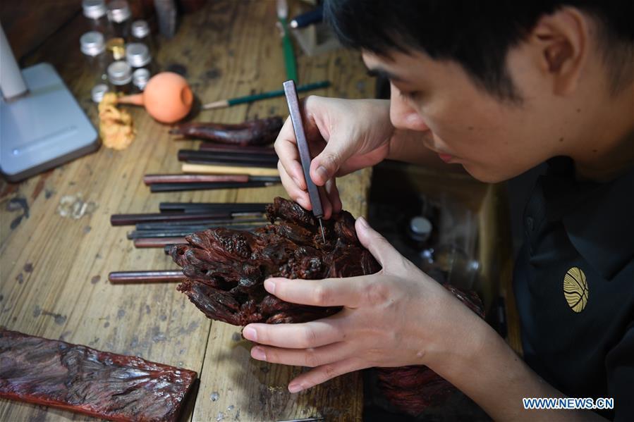 Lin Jianjun makes wood carving at a studio in Putian, southeast China\'s Fujian Province, Oct. 23, 2018. Lin Jianjun, who learnt wood carving at the age of 16, has studied the making skill of this traditional artwork for more than 20 years. In 2014, Lin got married with Chen Qin. The wife was influenced by her husband and got interested in wood carving. She developed the wood carving by combining a traditional skill to make wood carving inlaid with gold and silver. The couple meanwhile try to promote the Putian wood carving by giving lessons, instructing apprentices and displaying their works to the public. In 2018, Lin was appointed as the inheritor of the wood carving skill, a provincial-level intangible cultural heritage. (Xinhua/Jiang Kehong)