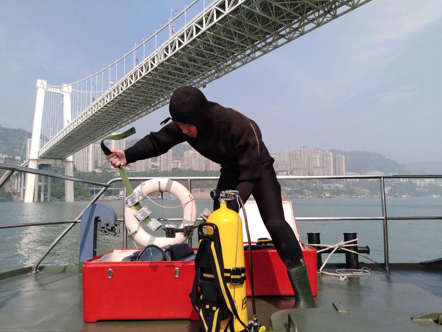 A diver from the armed police force stationed in Chongqing prepares to search the water on Sunday. (Photo by ZHOU YUKAI/FOR CHINA DAILY)

The driver of the car, identified as Kuang, was taken to the hospital with soft tissue injuries. The bus driver, surnamed Ran, is among the missing, the police said.

The cause of the accident is under investigation.

A rescue worker at the site said that the bridge stands more than 50 meters above the water and that the bus had sunk 68 meters below the surface.

Firefighters, public security officials and police officers were working on a plan to recover the bus.

The Ministry of Emergency Management dispatched 11 professional divers, a medical worker capable of deep diving and a salvage boat to assist in the rescue operation.

vThe four-lane Second Yangtze River Bridge opened to traffic in June 2003. It carries a daily average of more than 60,000 vehicles and over 200,000 commuters, according to the Wanzhou government.