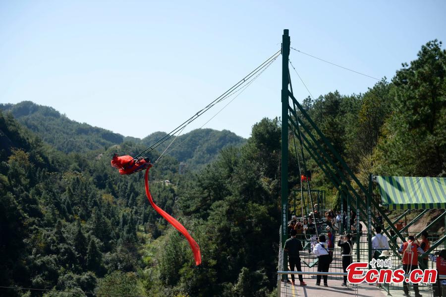 A woman dons a wedding dress to pose for a photo while sitting on a swing that is built close to a cliff at the Shiniuzhai National Geological Park in Pingjiang County, Central China\'s Hunan Province, Oct. 28, 2018. (Photo: China News Service/Yang Huafeng)