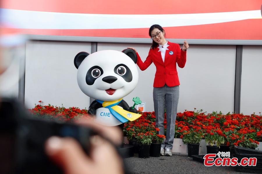 A volunteer for the upcoming China International Import Expo (CIIE) poses for a photo with the mascot \