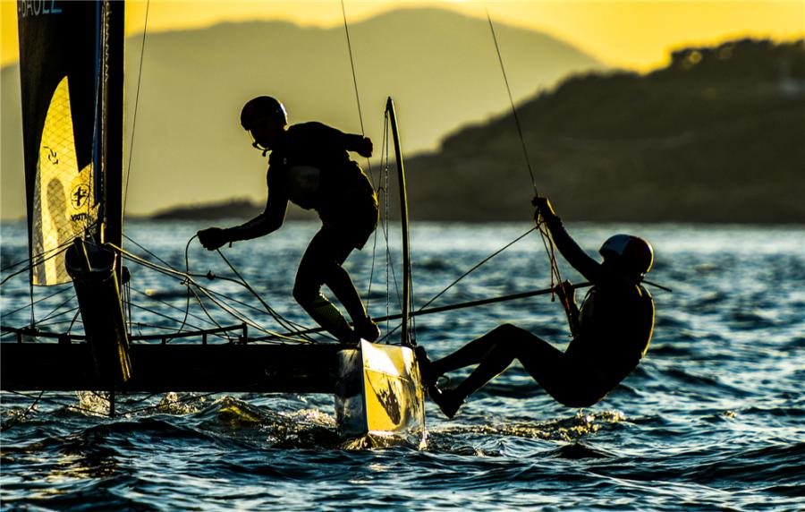 Sailors steer a two-man catamaran as their silhouettes are highlighted during the 2018 Extreme Sailing Series Qingdao Mazarin Cup. (Photo by Zhong Weihua/for chinadaily.com.cn)