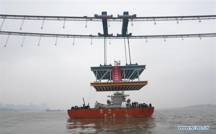 A 1,000-tonne steel beam is lifted to be installed at the construction site of the Yangsigang Bridge across the Yangtze River in Wuhan, capital of central China\'s Hubei Province, on Nov. 15, 2018. Construction of a double-deck suspension bridge with the longest span in the world is expected to be completed in October 2019, said an engineer working on the project. The bridge, with a 1,700-meter-long main span across the Yangtze River in Wuhan, saw the first steal beam installed for the bridge deck Thursday. (Xinhua/Cheng Min)
