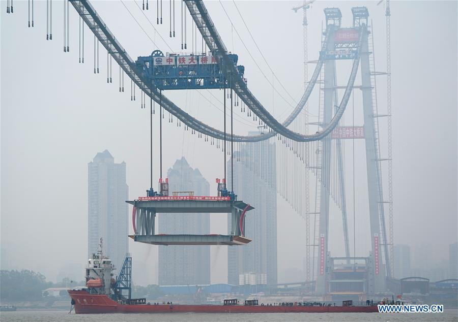 A 1,000-tonne steel beam is lifted to be installed at the construction site of the Yangsigang Bridge across the Yangtze River in Wuhan, capital of central China\'s Hubei Province, on Nov. 15, 2018. Construction of a double-deck suspension bridge with the longest span in the world is expected to be completed in October 2019, said an engineer working on the project. The bridge, with a 1,700-meter-long main span across the Yangtze River in Wuhan, saw the first steal beam installed for the bridge deck Thursday. (Xinhua/Cheng Min)