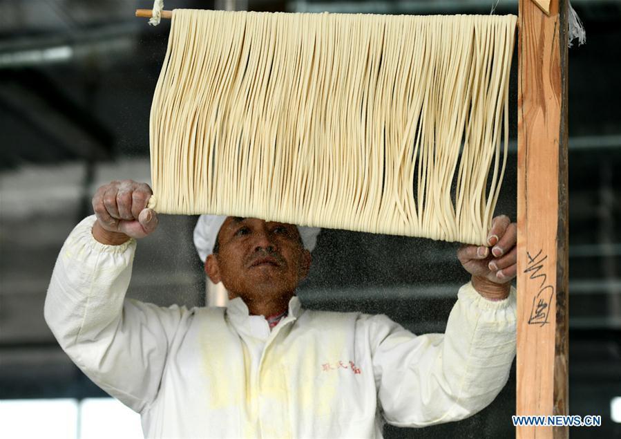 A worker makes noodles in a factory in Gengjiazhuang Village of Gaocheng District in Shijiazhuang, capital of north China\'s Hebei Province, Nov. 23, 2018. The fine dried noodle produced in Gongcheng, formerly article of tribute to the imperial family, is famous for its thin but hollow strings that is a result of more than ten working procedures. (Xinhua/Zheng Yaning)