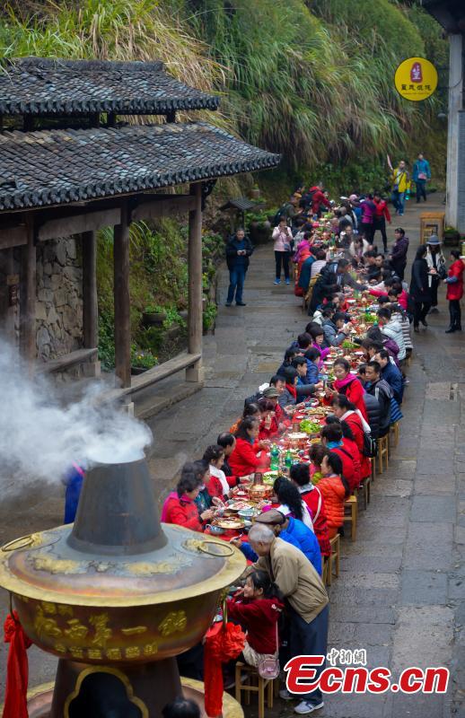 A hot-pot banquet is held on a street in Huangling Ancient Village in Wuyuan County, East China\'s Jiangxi Province, Dec. 22, 2018. The centerpiece of the long-table banquet, a traditional manner in which to celebrate some major festivals and entertain guests, is a giant copper pot measuring three meters in height and two meters in diameter. Visitors, including some from Singapore and Malaysia, joined the feast, where the tables extended for 100 meters. (Photo: China News Service/Fang Huabin)