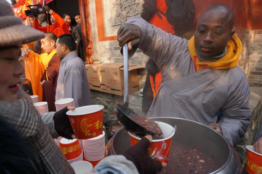 Visitors share Laba congee handed out for free during an event taking place in front of the temple\'s Shaolin Medicine health unit, Jan. 13, 2019. The congee was cooked according to a traditional recipe and included five types of beans as well as more than 20 minor ingredients. Buddhist temples across China have started handing out free Laba congee, a special meal served during the Laba Festival, which falls on the eighth day of the 12th lunar month and ushers in China\'s Lunar New Year celebrations. (Photo: China News Service/Han Zhangyun)