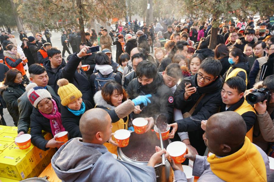 Visitors share Laba congee handed out for free during an event taking place in front of the temple\'s Shaolin Medicine health unit, Jan. 13, 2019. The congee was cooked according to a traditional recipe and included five types of beans as well as more than 20 minor ingredients. Buddhist temples across China have started handing out free Laba congee, a special meal served during the Laba Festival, which falls on the eighth day of the 12th lunar month and ushers in China\'s Lunar New Year celebrations. (Photo: China News Service/Han Zhangyun)