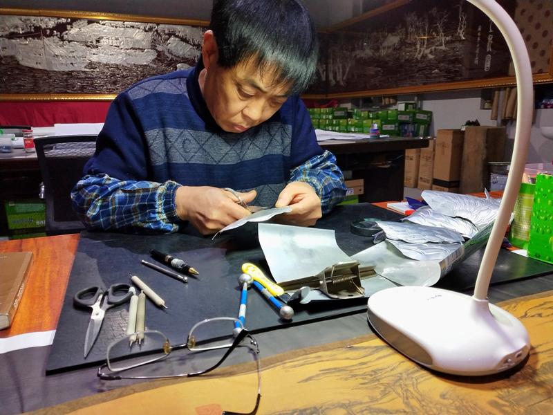 Gao Baoan cuts metal cans into pieces for his artwork. (Photo provided to chinadaily.com.cn)