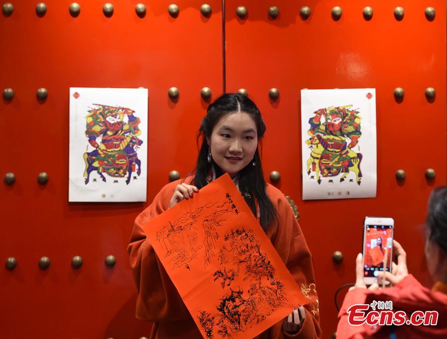 A woman shows a picture outside the Lao She Tea house in Beijing, where a Spring Festival paintings exhibition is being held, Jan. 27, 2019. The exhibition, organized by the Ministry of Culture and Tourism and Prince Gong\'s Mansion, presented representative traditional paintings of the Lunar New Year from across the country, and will run from Jan. 28 to Feb. 28. (Photo: China News Service/Hou Yu)