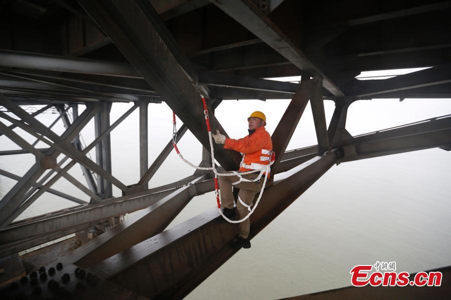 A technician conducts a routine safety check on the Jiujiang Yangtze River Bridge, a major connection of the Beijing-Kowloon Railway in Jiujiang City, East China\'s Jiangxi Province during the travel peak of the Spring Festival. Despite the wind and vibration caused by the passing trains, they continued working in baskets hung under the bridge\'s girder, about 20 meters above the rolling Yangtze River. (Photo: China News Service/Ding Bo)