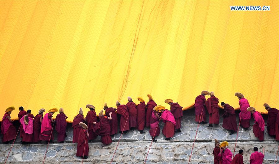 Lamas of the Labrang Monastery unroll the huge thangka scroll painting bearing the image of the Buddha covered by a large yellow curtain during the annual \