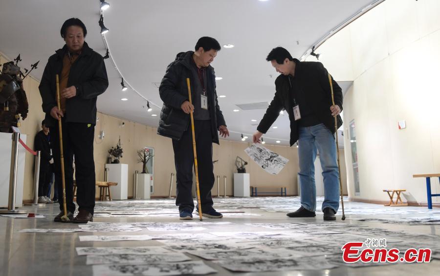 Judges use bamboo sticks to help them review paintings by applicants to the Shandong University of Arts in Jinan City, Shandong Province, Feb. 28, 2019. More than 10,000 paintings were placed in a corridor for judges to grade. (Photo: China News Service/Zhang Yong)